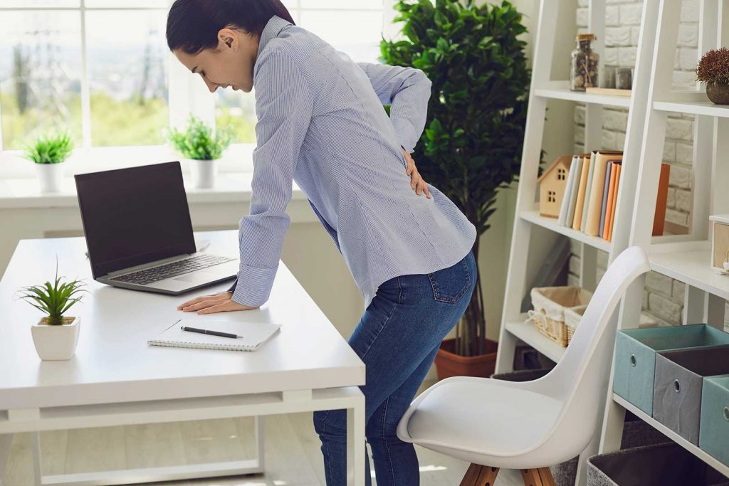 woman in an office holding her back in pain